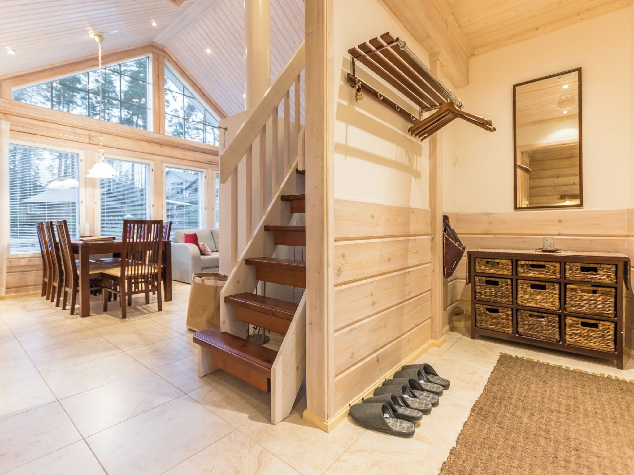 Une pièce spacieuse avec un escalier en bois, un coin repas comprenant des chaises et une table, et une grande fenêtre offrant une vue sur les arbres.
