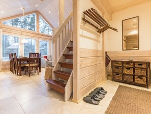 A spacious room with a wooden staircase, a dining area with chairs and a table, and a large window providing a view of trees.