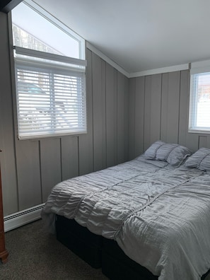 Un dormitorio con una cama, dos ventanas y un radiador.