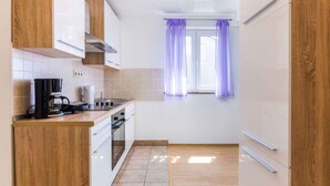 Une cuisine de taille réduite avec des meubles blancs, une machine à café et une fenêtre ornée de rideaux violets.