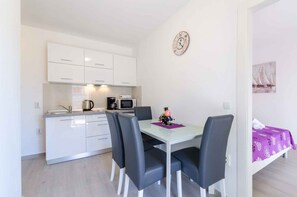 Compact kitchenette with microwave, coffee maker, and dining area with glass table and four chairs.
