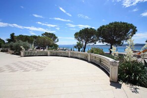 A curved outdoor terrace with a checkered floor, surrounded by a balustrade, overlooking a body of water and trees.