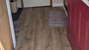 Un hall d’entrée au plancher de bois, avec une porte rouge, une fenêtre à cadre blanc et un carillon.
