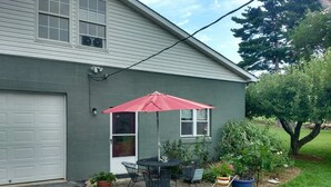Une maison d’habitation avec un garage, une terrasse avec une table et des chaises, et des plantes en pot.