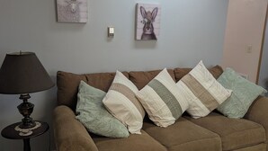 Un salon avec un canapé marron, une lampe, une petite table ronde et deux œuvres d’art accrochées au mur.