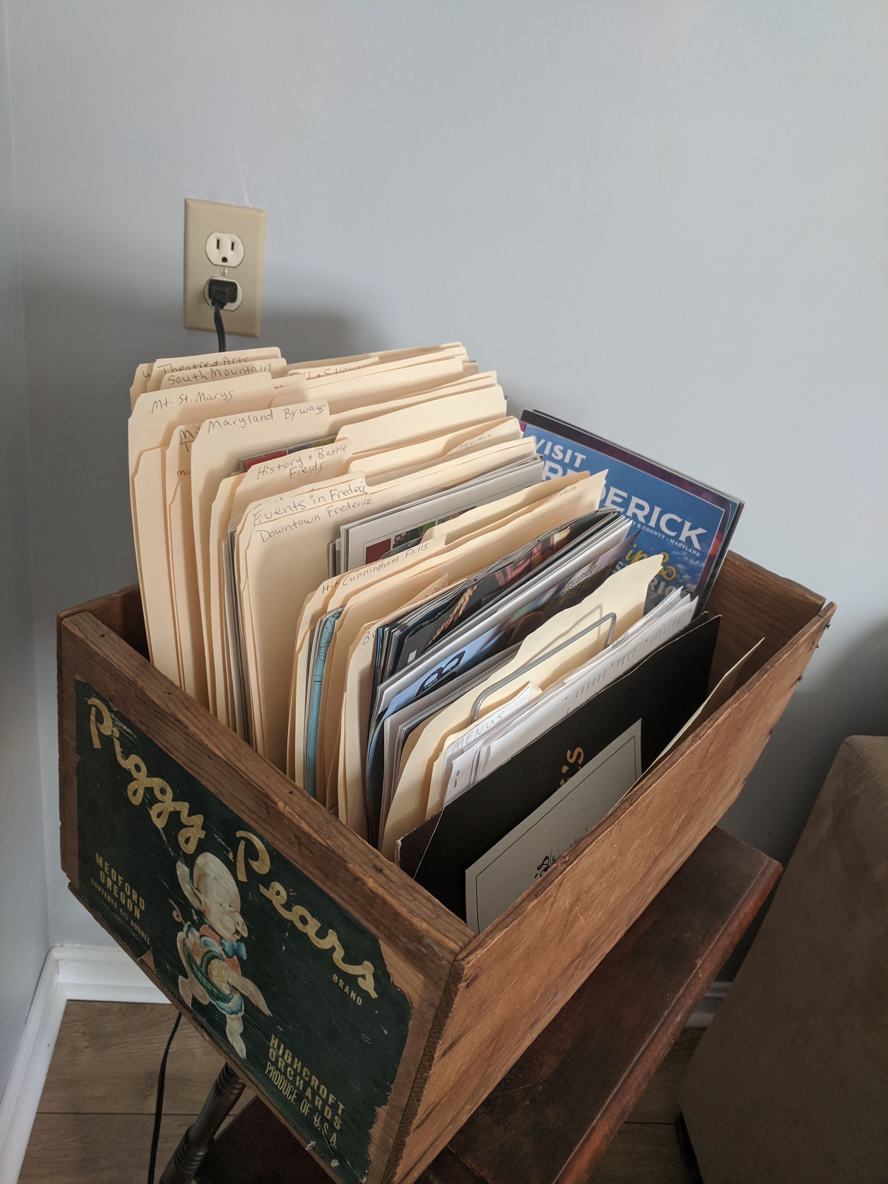 Un archivador de madera lleno de carpetas y un libro titulado 'Visit Maryland'.