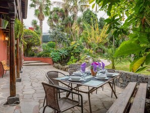 Une terrasse extérieure avec un sol en pierre, des chaises et des tables en osier, le tout disposé pour les repas.