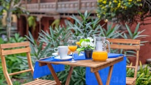 Una mesa de madera dispuesta con una taza blanca, un vaso de zumo de naranja, una jarra de zumo de naranja y una pequeña planta en maceta.