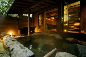 A hot spring area with a wooden deck, a stone pathway, and a glass door leading to an interior space. - Tetsuka Ryokan (Satsuma)