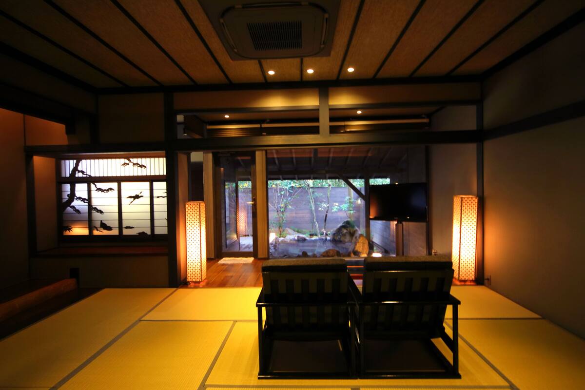 Une pièce de style japonais traditionnel, avec un sol recouvert de tatamis, une table basse et une vue sur un bassin à carpes koï, visible à travers une porte coulissante.