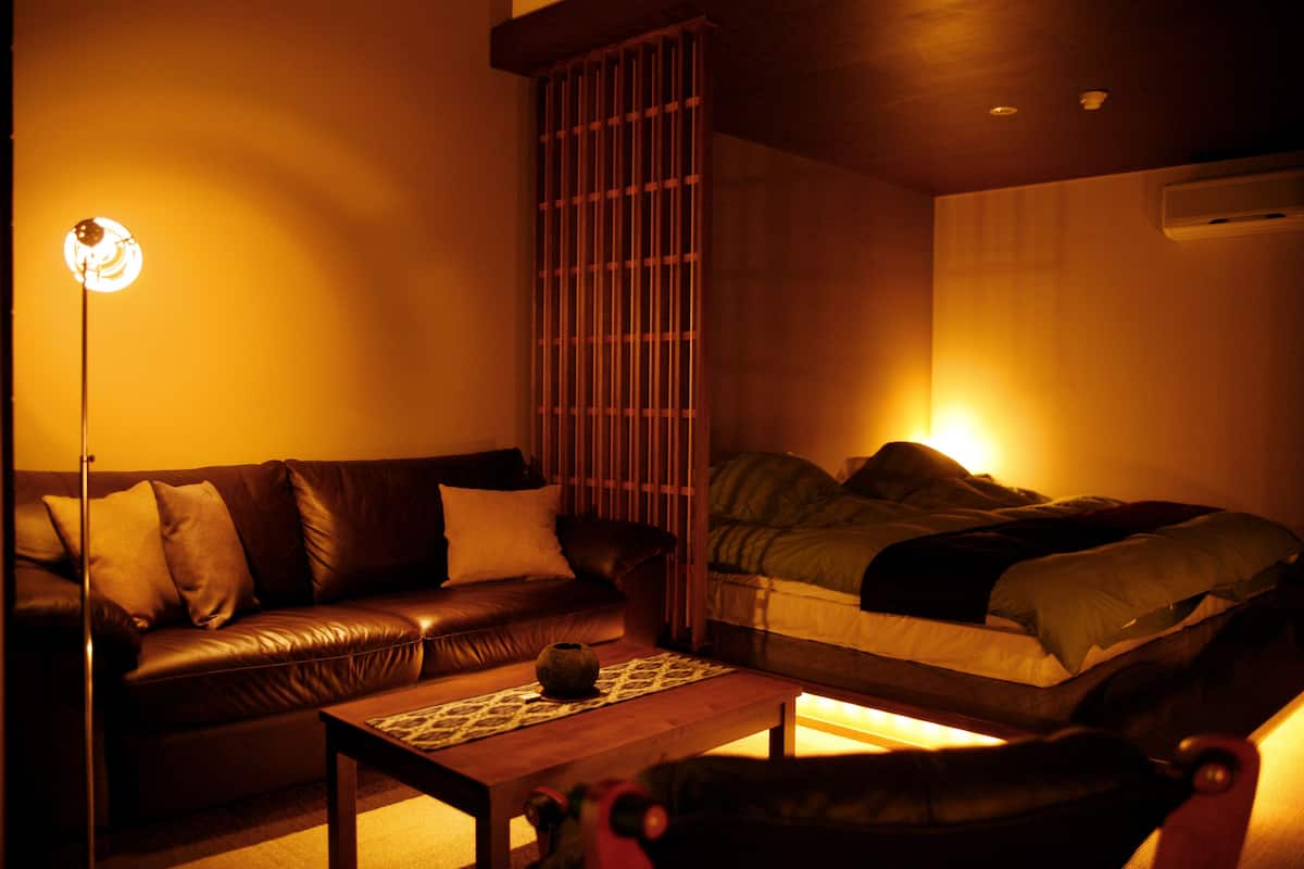 Un salon chaleureux avec un canapé en cuir, une table basse en bois et un lit recouvert d’une couverture verte.