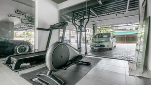 Un gimnasio con equipo de ejercicio, un coche al fondo y vistas al exterior a través de amplias ventanas.