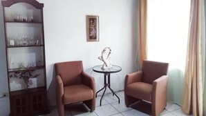 A room with two brown armchairs, a small round table with a sculpture, a wooden cabinet with glass shelves, a framed picture on the wall, and a window with curtains. - ARCO House, La Marina. Saint Charles (San Carlos)