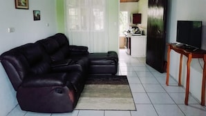 A living room with a sectional sofa, a television on a wooden stand, and a kitchen in the background. - ARCO House, La Marina. Saint Charles (San Carlos)
