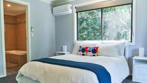 Een slaapkamer met een groot bed, een raam met uitzicht op bomen, een douchegedeelte en een airconditioning.
