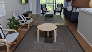 Een moderne woonkamer met een bank, twee fauteuils, een salontafel en een aan de muur bevestigde televisie.