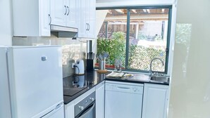 Een moderne keuken met witte kasten, een vaatwasser, een fornuis en een raam met uitzicht op een tuin.