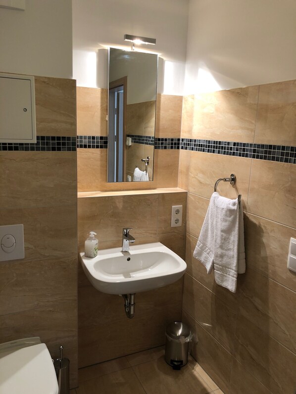 A bathroom with a sink, mirror, towel rack, and a trash can. - Nature & relaxation meets style & comfort - living in Werder (Werder (Havel))