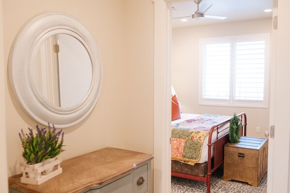 A bedroom with a bed, a bedside table, a dresser, a mirror, and a window with blinds.
