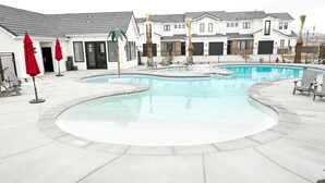 Ein Pool mit geschwungener Form, umgeben von Liegestühlen und Sonnenschirmen.