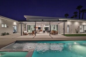 Uma casa moderna com piscina, móveis de jardim e área externa coberta.