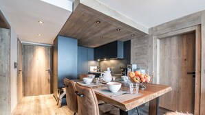 A modern kitchen with wooden cabinetry, a dining table set with white dishes, and a fruit bowl. - Winter Courchevel / Phoenix 502, proche commerce (Courchevel)