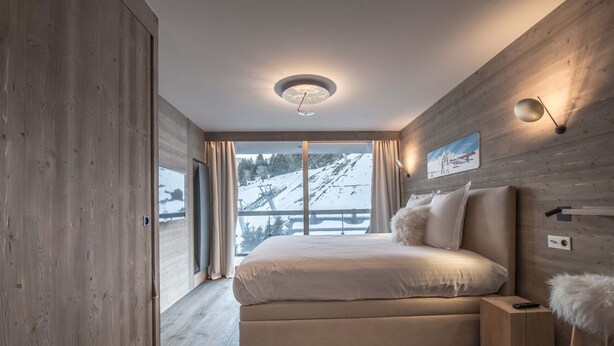 A modern bedroom with a large bed, wooden walls, a view of a snowy mountain, and a ceiling light. - Winter Courchevel / Phoenix 502, proche commerce (Courchevel)
