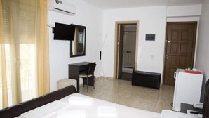 A hotel room with a bed, a desk, a chair, a small table, a TV, an air conditioner, a door, and a shower area. - Pyrgos Sofokleous (Lesvos)