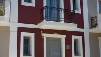 Un edificio de dos pisos con fachada roja y blanca, una puerta gris y un balcón con barandillas negras.