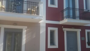 A two-story building with a red and white facade, balconies with metal railings, and a tiled entrance area. - Pyrgos Sofokleous (Lesvos)