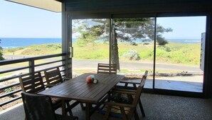 Un área de estar al aire libre techada con mesa y sillas, con vista a un paisaje costero.