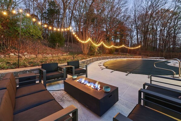 Un espace extérieur aménagé avec un foyer, des guirlandes lumineuses et une terrasse incurvée.