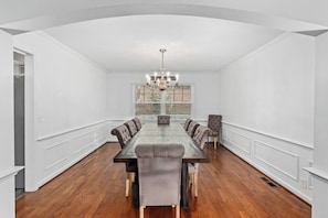 Une salle à manger spacieuse, avec une longue table, de nombreuses chaises et un lustre.