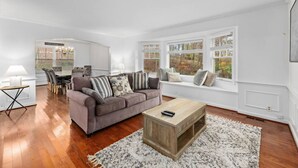 Sala de estar com sofá, mesa de centro e vista através de amplas janelas.