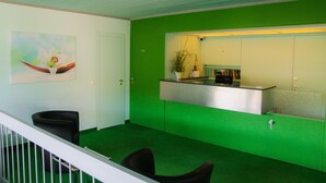 Un área de recepción con una pared verde, un cuadro de una flor, un mostrador de recepción y una barra con una planta.