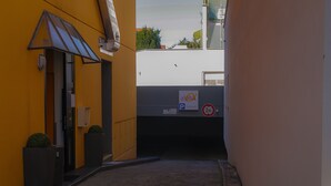 Un estrecho callejón con un edificio amarillo a la izquierda, uno blanco a la derecha y un letrero que indica un área de estacionamiento.