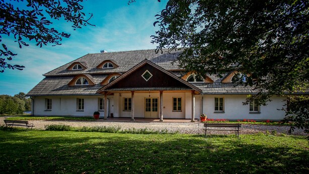 A two-story building with a symmetrical facade, a central entrance with a covered porch, and a sloped roof with dormer windows. - Dwor Strzyzew (gmina Kampinos)