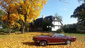 A red convertible car parked on a leaf-covered ground with a white house in the background. - Dwor Strzyzew (gmina Kampinos)