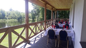An outdoor dining area with tables set for a meal, overlooking a lake. - Dwor Strzyzew (gmina Kampinos)