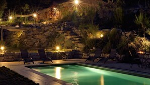 A nighttime outdoor pool area with stone walls, lounge chairs, and ambient lighting. - greenery in the chestnut grove. (Tasso)