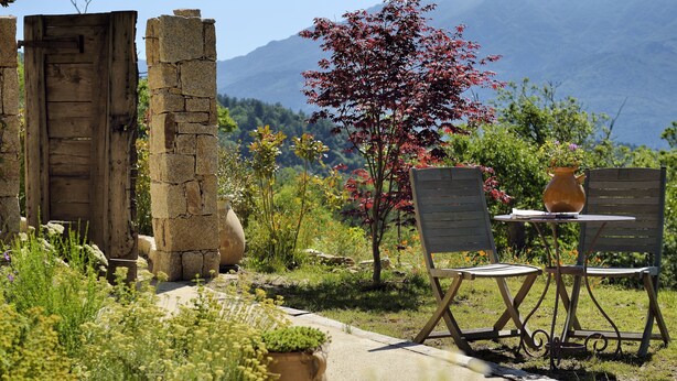 A rustic outdoor seating area with stone pillars, a wooden door, and a table with chairs. - greenery in the chestnut grove. (Tasso)