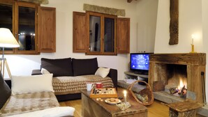 A cozy living room with a sofa, a wooden coffee table with chess pieces, a television, and a fireplace. - greenery in the chestnut grove. (Tasso)
