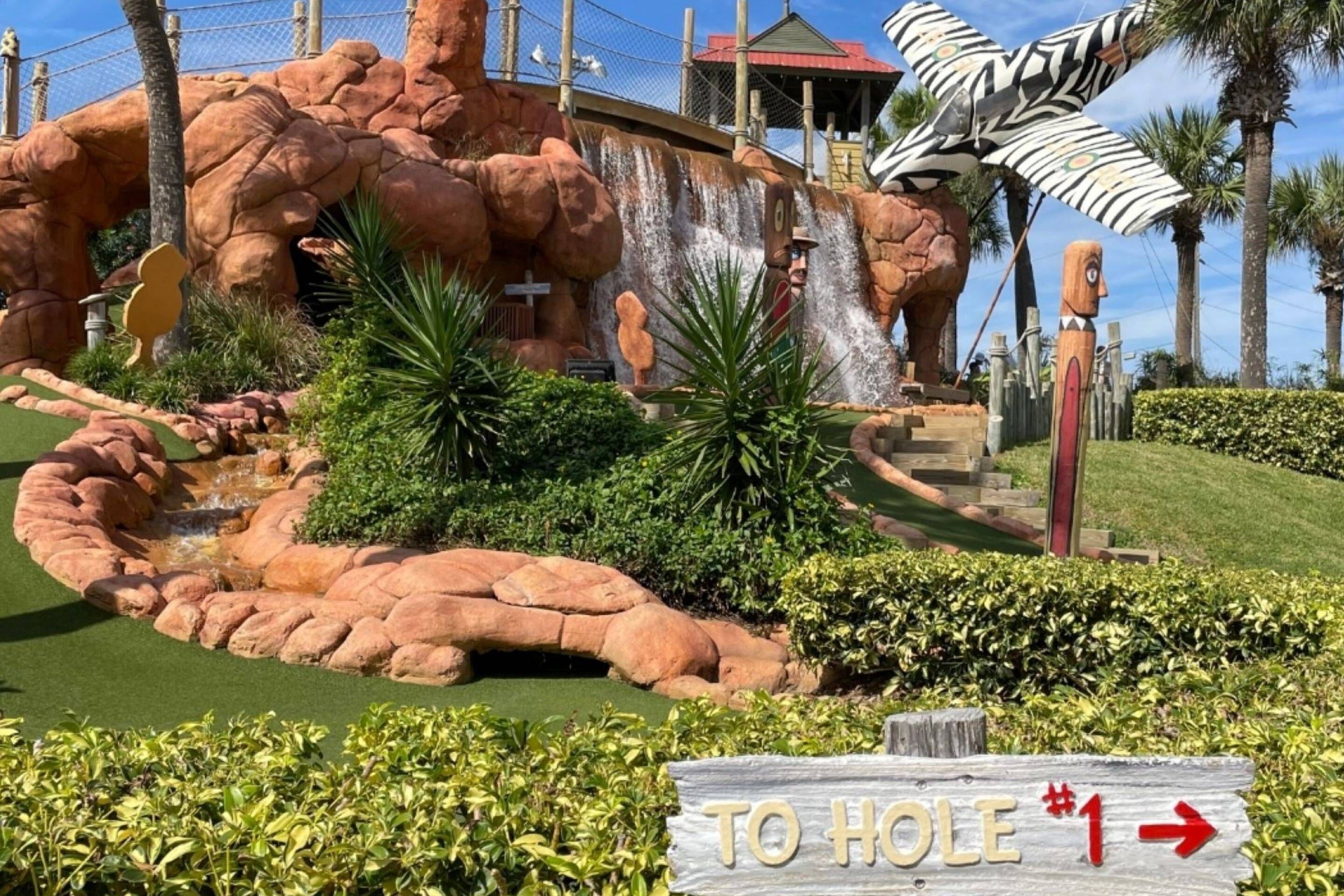A landscaped area with a rock formation, a small waterfall, and a sign indicating a hole.