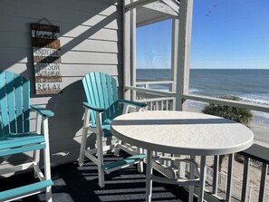 Un balcon avec deux fauteuils Adirondack turquoise et une petite table ronde, d’où l’on a une vue sur l’océan.