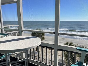 Un balcon avec vue sur l’océan et la plage, comprenant une table et des chaises.