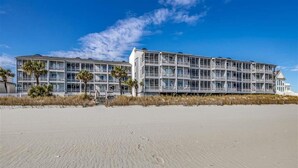 Ett hotell vid stranden med flera balkonger, en sandstrand framför och en klarblå himmel.