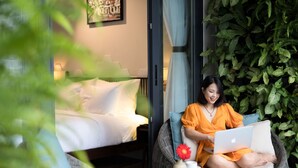 A room with a bed, a wicker chair, and a green wall with plants. - Volar de Faifo Villa (Da Nang)