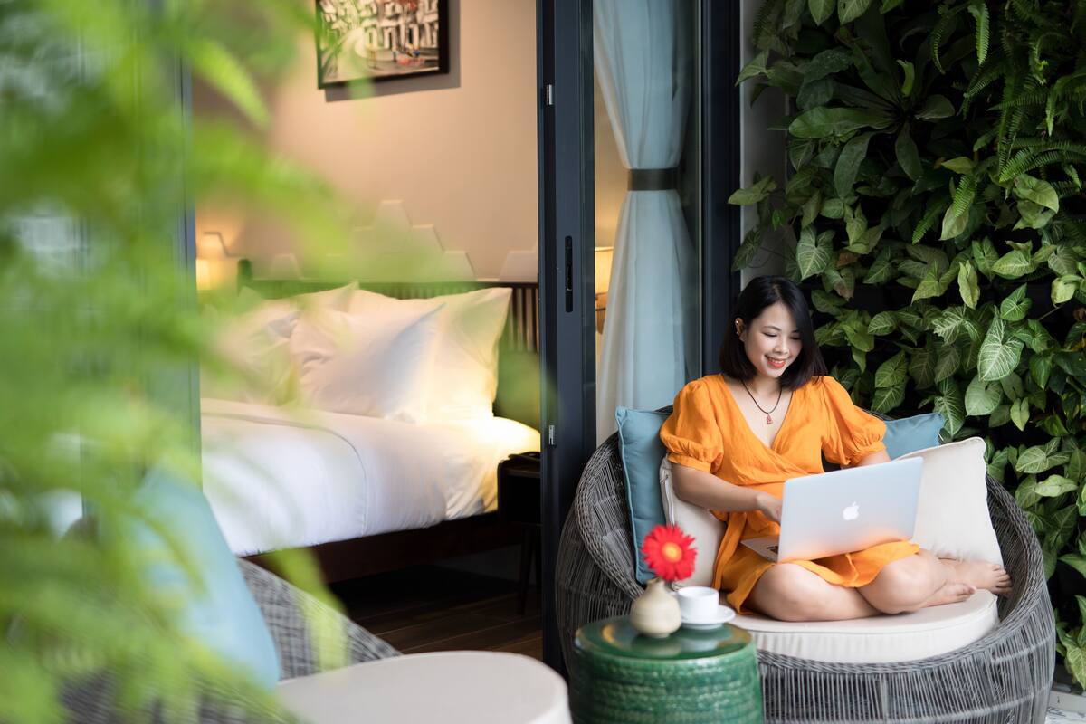 A room with a bed, a wicker chair, and a green wall with plants.