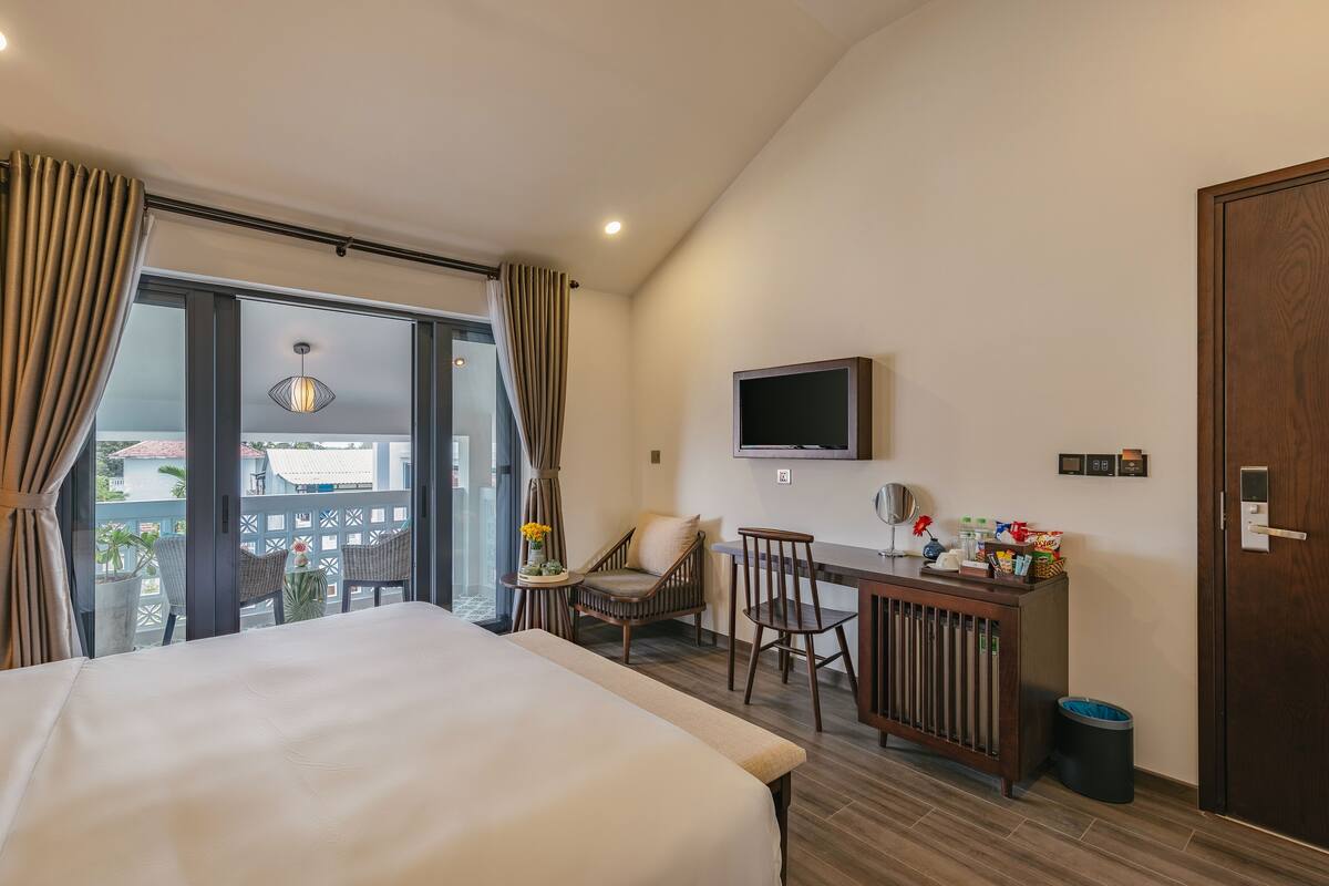 A hotel room with a bed, a desk with a TV, a chair, and a view of the outside.