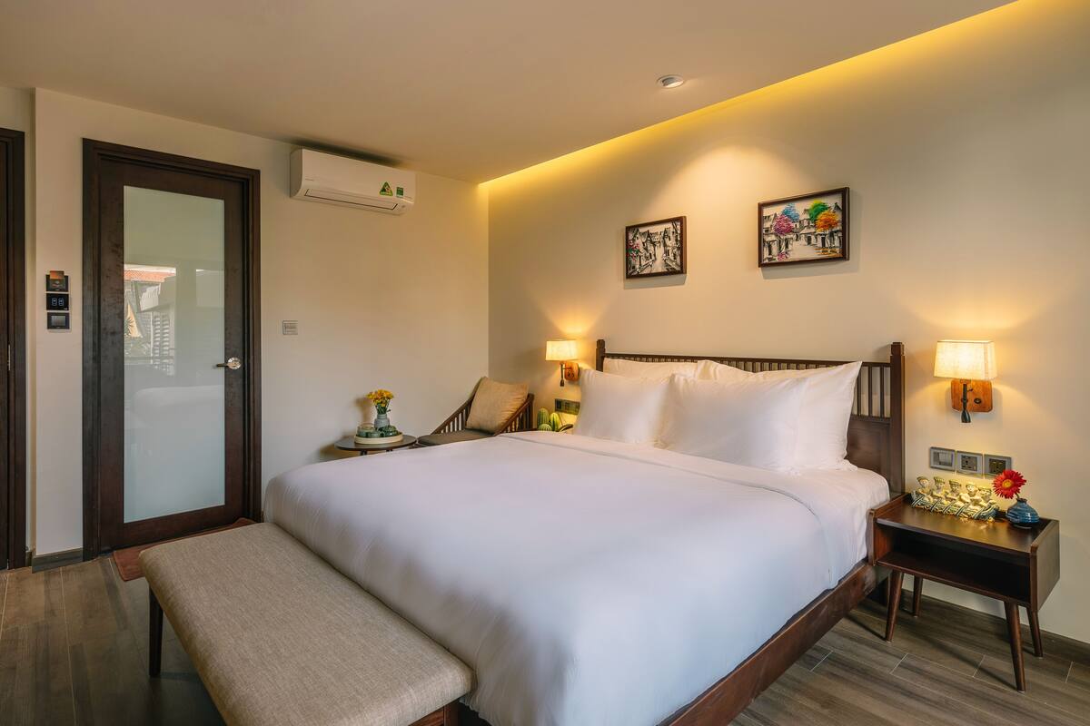 A hotel room with a large bed, bedside tables with lamps, a bench, and artwork on the walls.